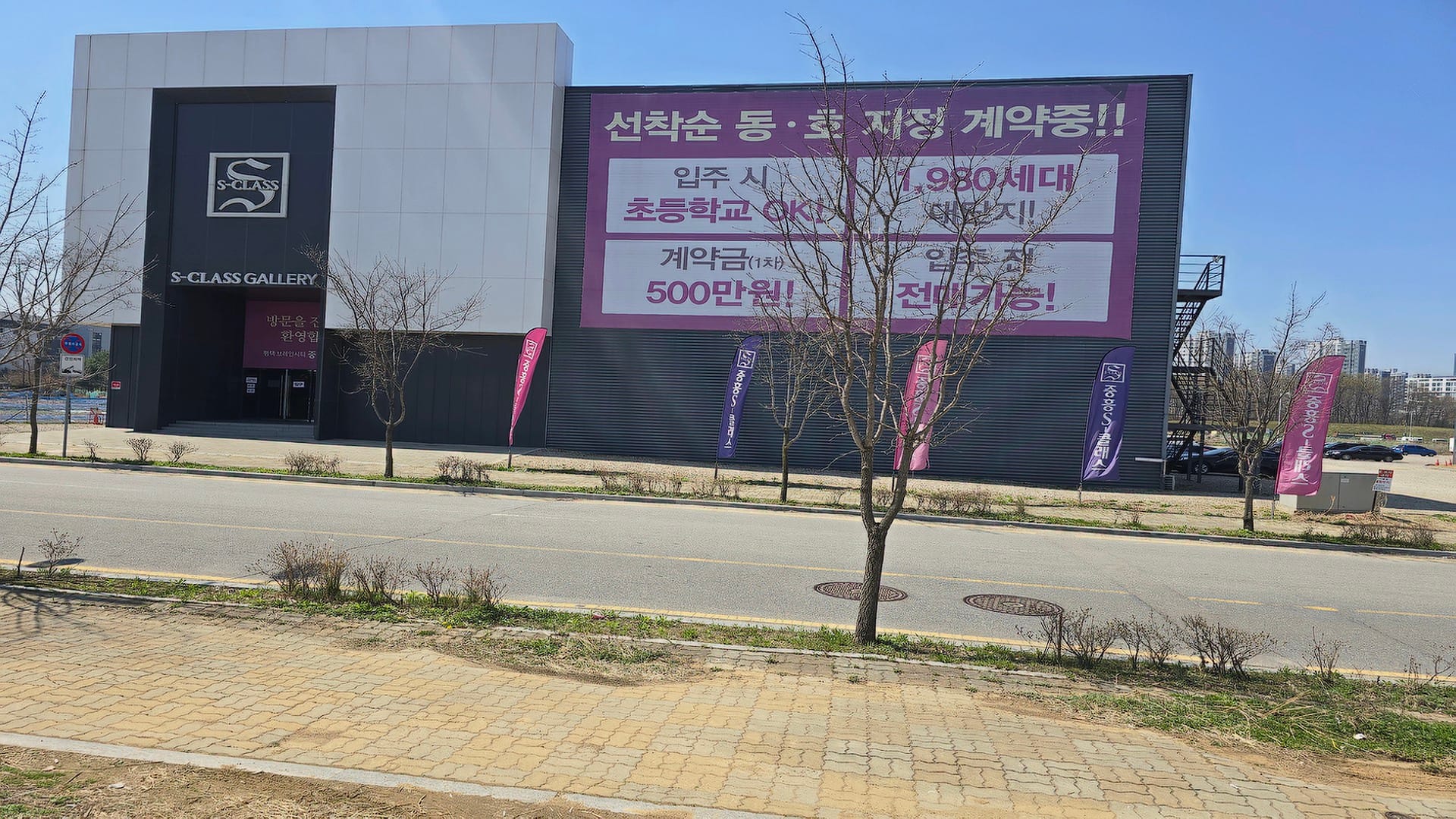 선착순 동호 지정 계약과 1차 계약금 500만 원 혜택을 홍보하는 대형 현수막이 설치된 평택 브레인시티 중흥S클래스 견본주택 외부 모습